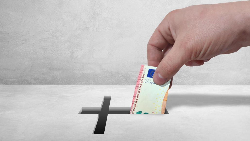 Hand steckt Geldschein in einen Schlitz mit Kreuz, Symbol für Spende